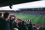 Fans cheer as players take the field at a vibrant football stadium, creating an electric atmosphere.